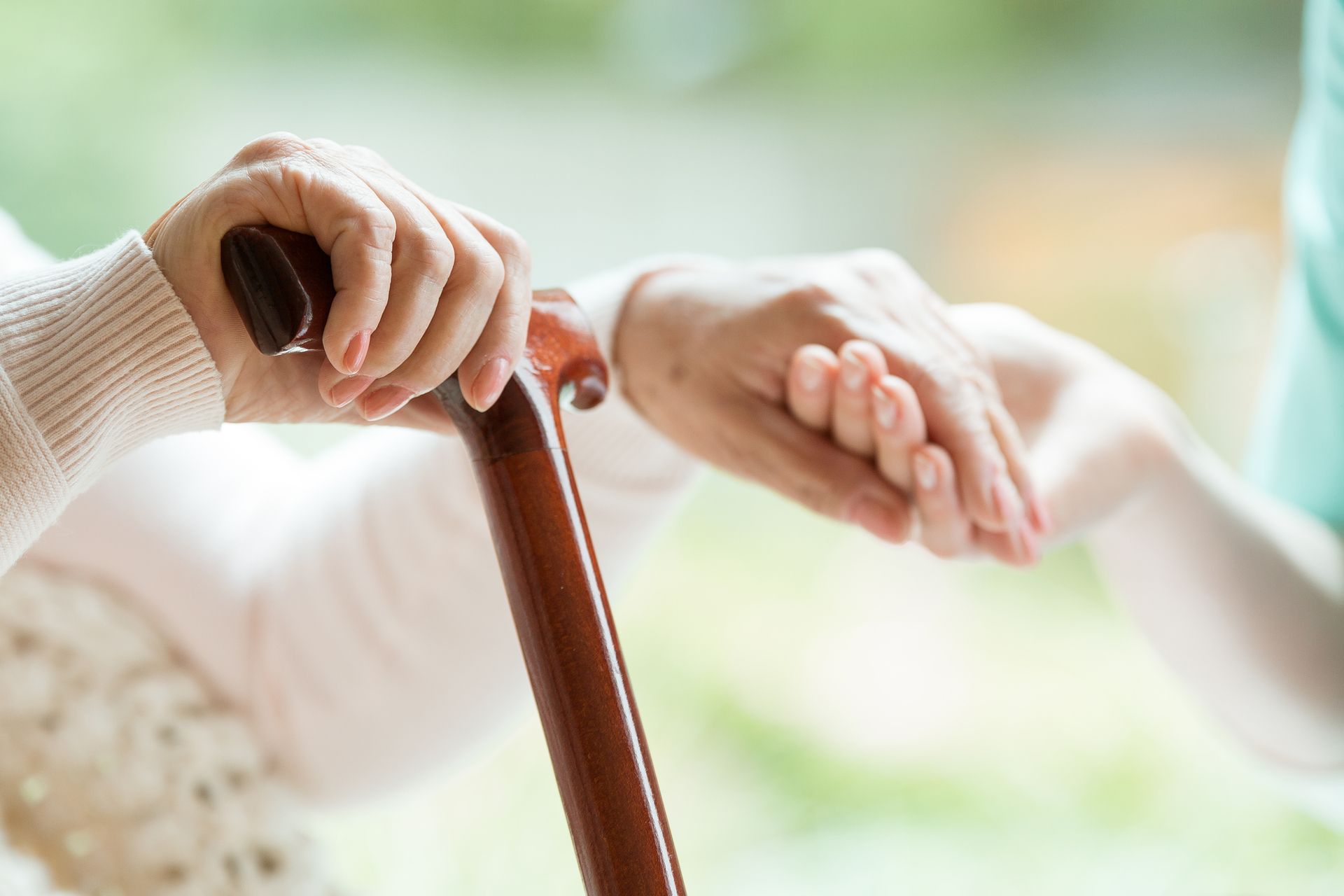 Nahaufnahme von zwei Händen - eine ältere Hand hält einen Gehstock, eine jüngere Hand liegt beruhigend darüber.